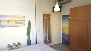 A bedroom with a bed, a wooden wardrobe, a painting of a sunset over water, and a green towel hanging on the wall. - Hotel Losanna (Cervia)