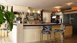 A bar area with a counter, bar stools, and a variety of bottles and glasses. - Hotel Losanna (Cervia)