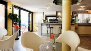 A modern interior with round tables and white chairs, a bar area in the background, and a large window providing natural light. - Hotel Losanna (Cervia)