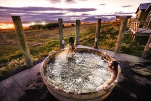 Una bañera de hidromasaje de madera con vistas a la puesta de sol y montañas al fondo.