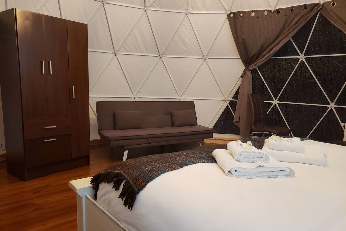 A bedroom with a bed, a wardrobe, a sofa, and a window with curtains.