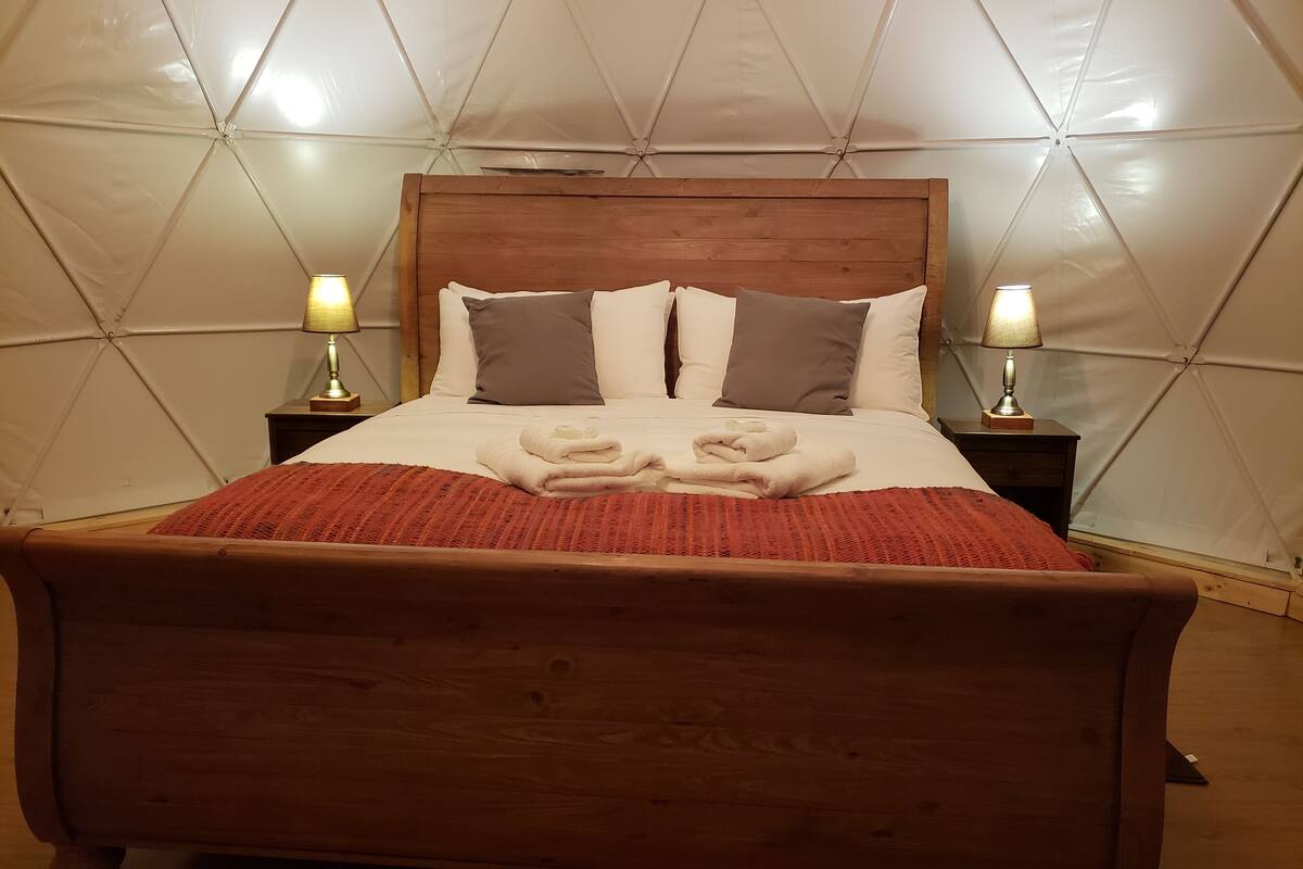 A bed with a wooden headboard, two bedside tables with lamps, and a red blanket.