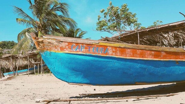 A boat named "CAP TOUBA" on a sandy beach with palm trees and a thatched-roof structure in the background. - Strathairn 110 by Pro Homes Jamaica (Kingston)