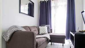 A living room with a brown sofa, a small ottoman, a TV stand, and a mirror on the wall. - Strathairn 110 by Pro Homes Jamaica (Kingston)