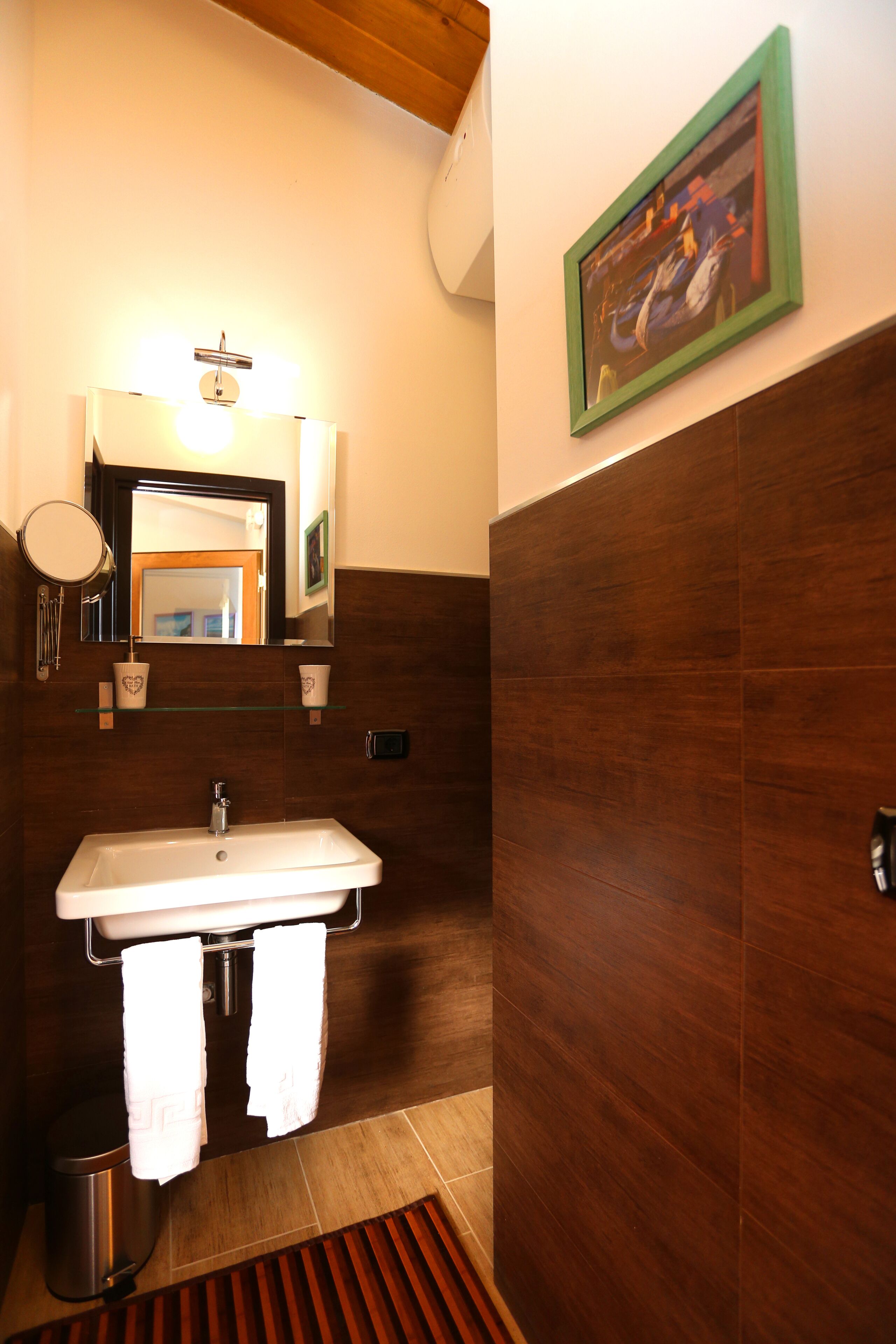 A bathroom with a white sink, two towels, a mirror, and a framed picture on the wall.