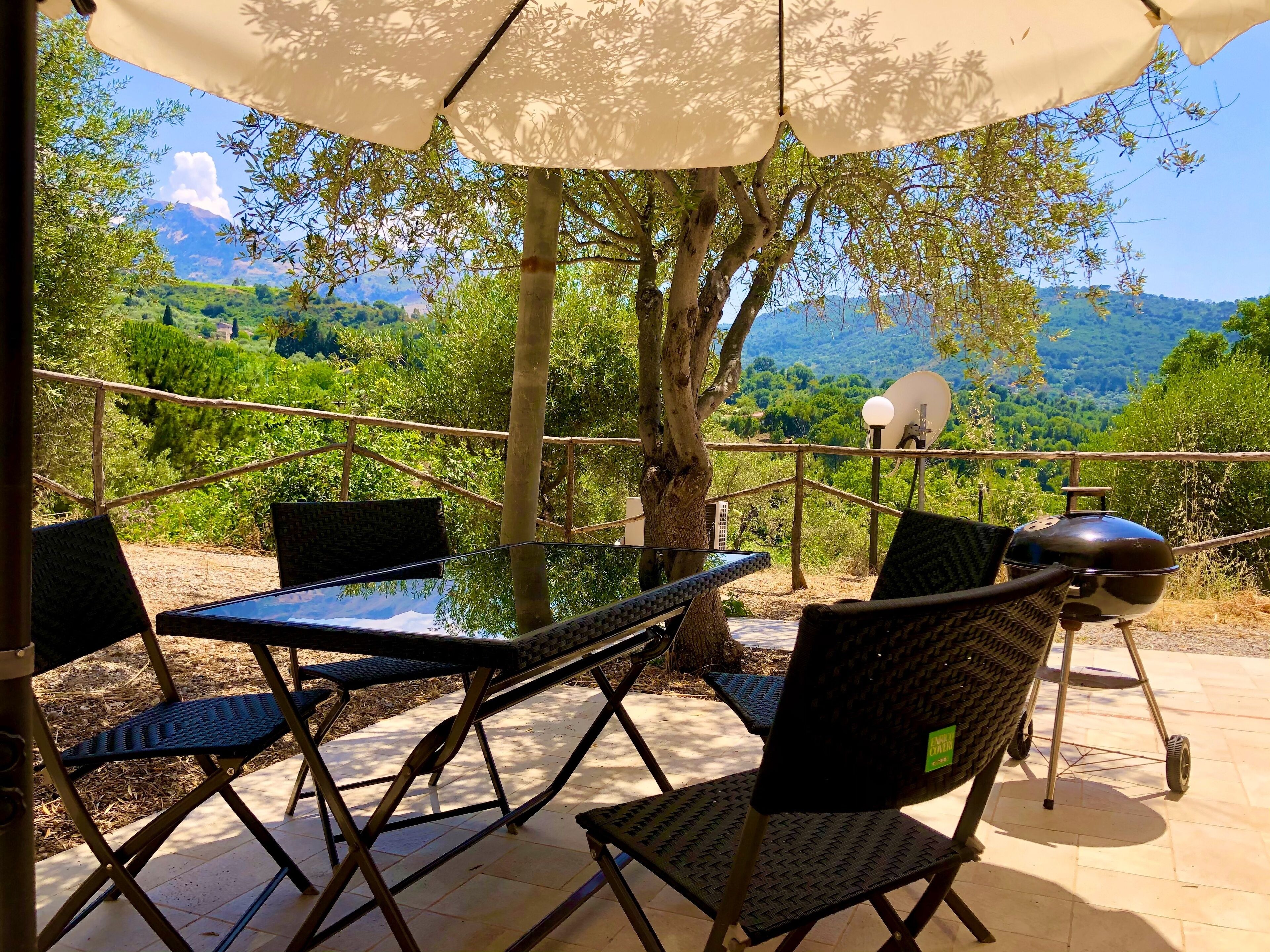 An outdoor patio with a table and chairs, a barbecue grill, and a view of a mountainous landscape.