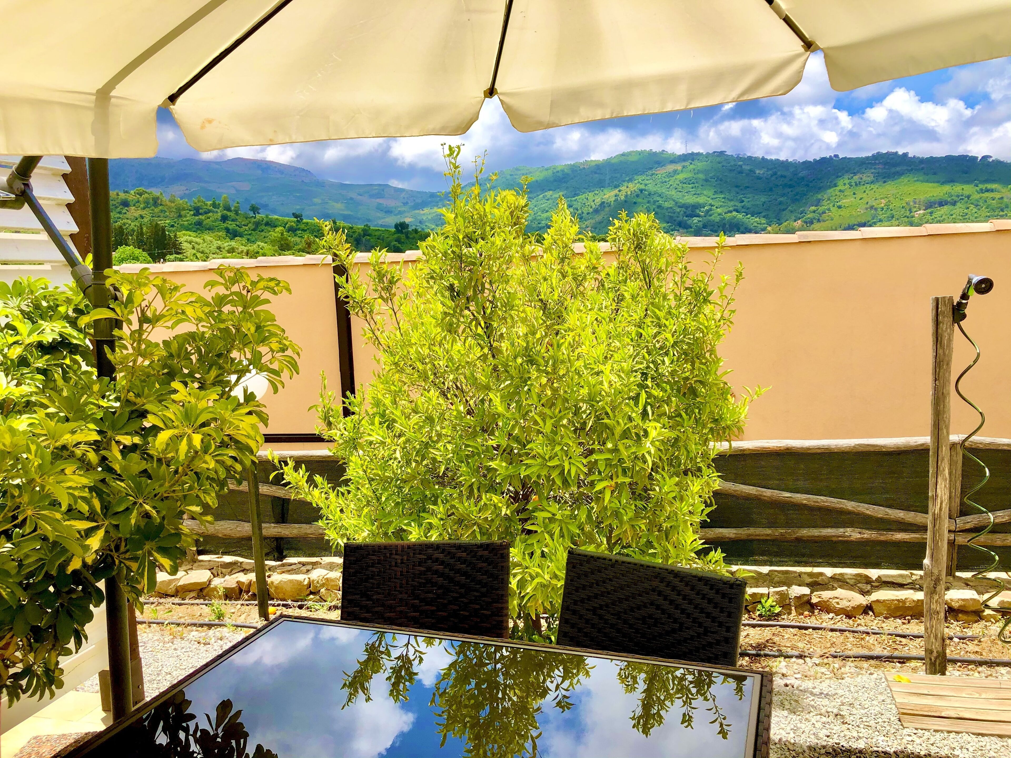 Une terrasse extérieure avec une table et des chaises sous une pergola, entourée de verdure et offrant une vue sur les collines.