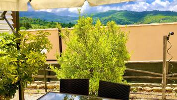 Une terrasse extérieure avec une table et des chaises sous une pergola, entourée de verdure et offrant une vue sur les collines.