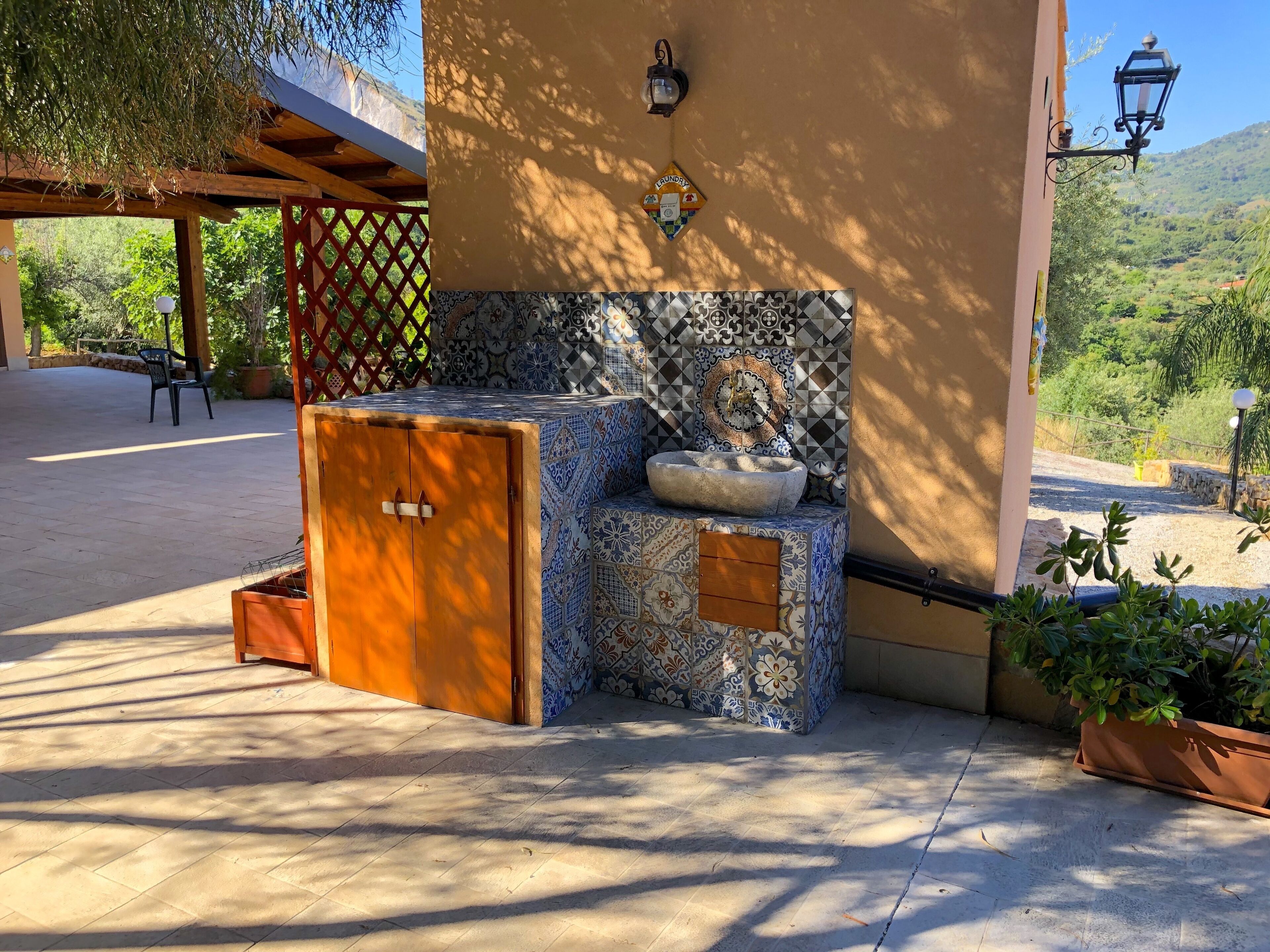 A sunlit outdoor seating area with a tiled bench, a wooden cabinet, and a wall-mounted light fixture.