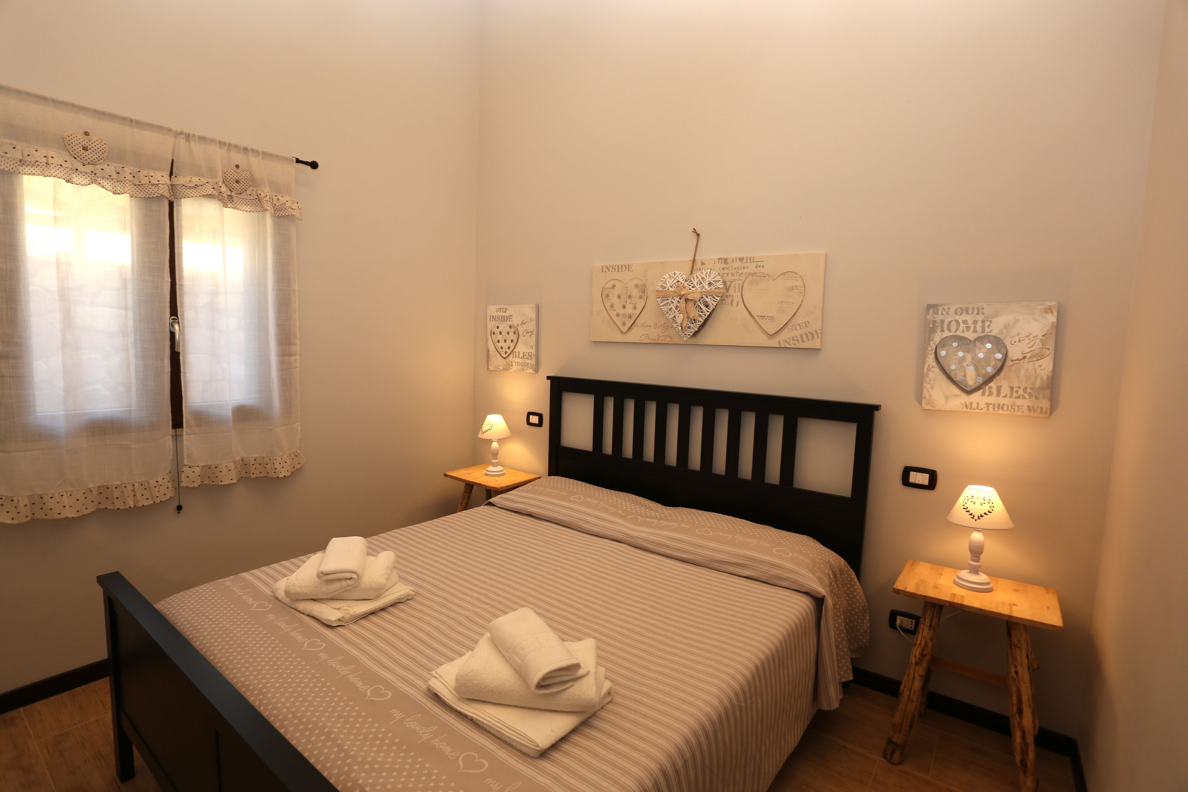 A neatly made bed with folded towels, a bedside table with a lamp, and heart-shaped decorations on the wall.
