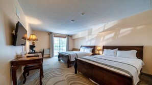 A hotel room with a large bed, a desk with a lamp, a TV, and a window with curtains. - Fullerton Manor Inn (Niagara Falls)