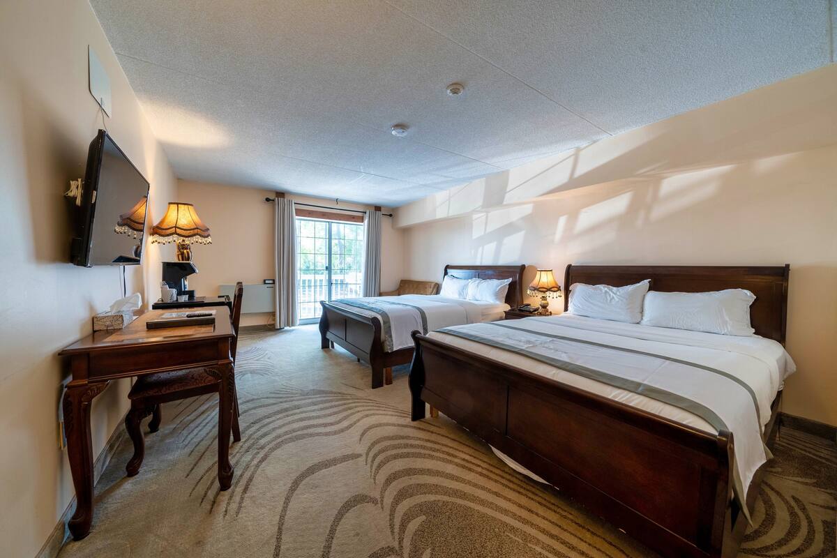 A hotel room with a large bed, a desk with a lamp, a TV, and a window with curtains.
