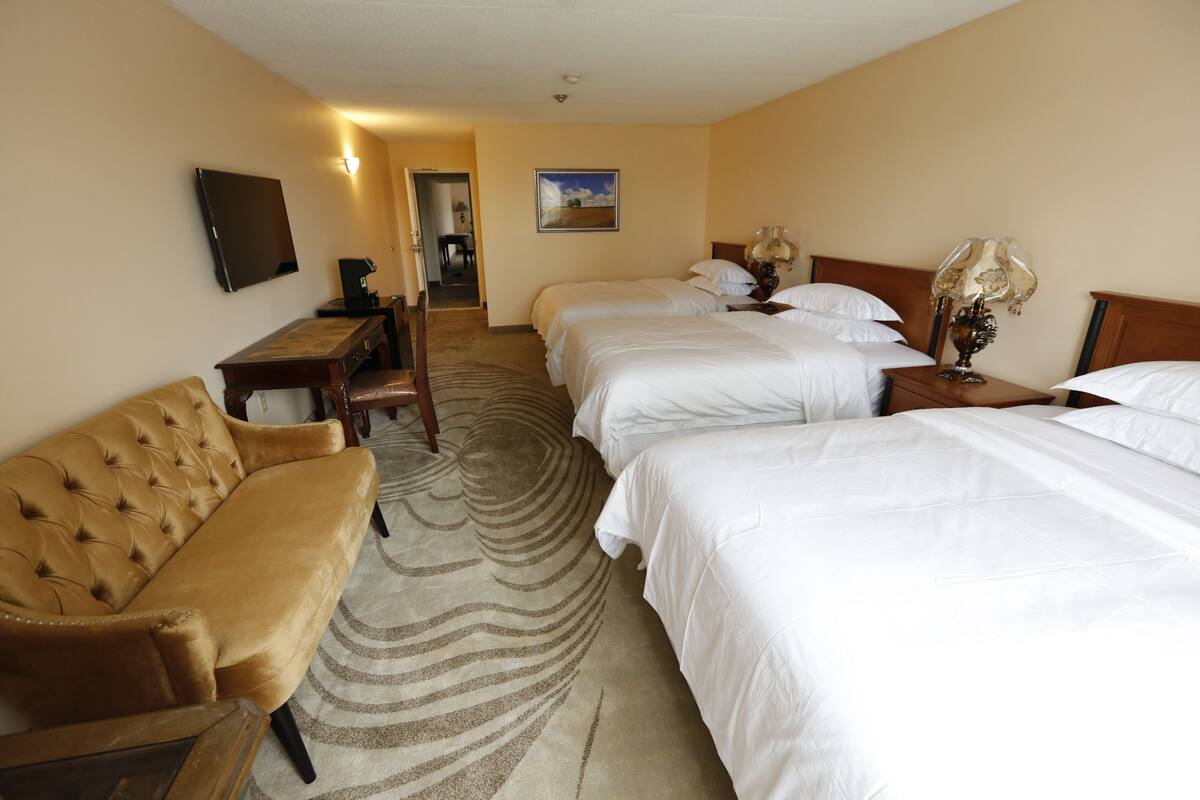 A hotel room with a sofa, two beds, a desk, and a TV.