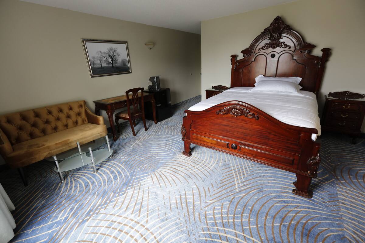A bedroom with a large bed, a wooden dresser, a chair, and a desk.