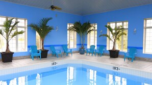 An indoor swimming pool with blue walls, potted palm trees, and blue chairs. - Fullerton Manor Inn (Niagara Falls)