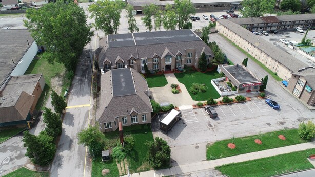 An aerial view of a building with a parking lot, green lawns, and a small outdoor seating area. - Fullerton Manor Inn (Niagara Falls)