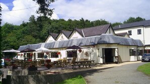 A building with a sign reading "Entrance" at the front. There are outdoor tables and chairs, and a car is parked nearby. - Carreg Bran Hotel (Llanfairpwllgwyngyll)