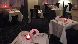 A dining area with tables set for two, each with candles, wine glasses, and cutlery. - Carreg Bran Hotel (Llanfairpwllgwyngyll)