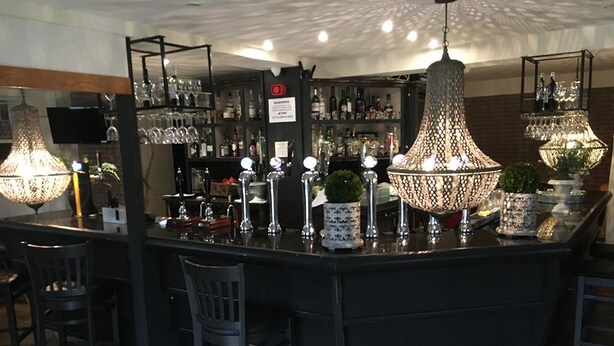 A bar area with a central island, bar stools, hanging light fixtures, and shelves with bottles and glasses. - Carreg Bran Hotel (Llanfairpwllgwyngyll)