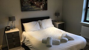 A neatly made bed with white linens and rolled towels, a painting on the wall, and a window with a view. - Carreg Bran Hotel (Llanfairpwllgwyngyll)