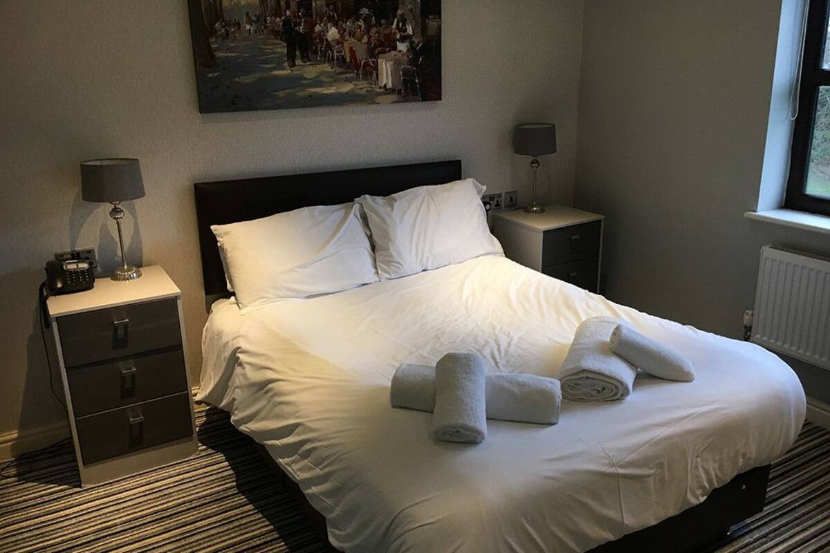 Un lit bien fait, avec du linge de lit blanc et des serviettes pliées, un tableau accroché au mur et une fenêtre offrant une belle vue.