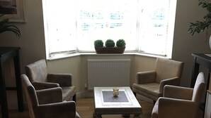 A living room with a bay window, a radiator, and three armchairs around a central coffee table. - Carreg Bran Hotel (Llanfairpwllgwyngyll)