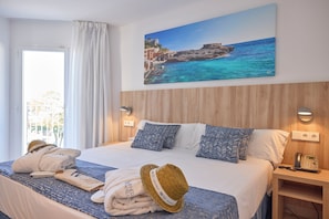A hotel room with a bed, two pillows, a nightstand with a phone, a painting of a coastal scene, and towels on the bed. - INNER Hotel Rupit - Adults Only (Santanyi)