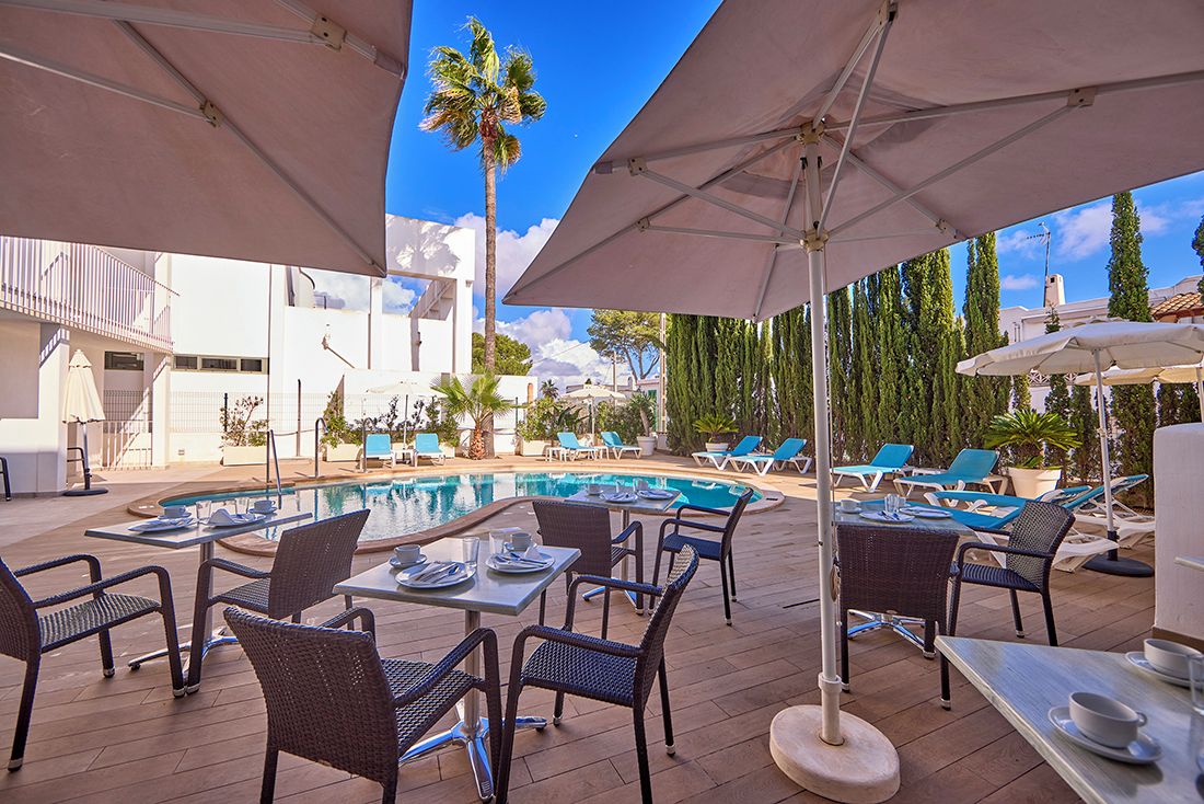 An outdoor pool area with lounge chairs and umbrellas, surrounded by buildings and trees.