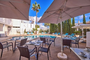 An outdoor pool area with lounge chairs and umbrellas, surrounded by buildings and trees. - INNER Hotel Rupit - Adults Only (Santanyi)