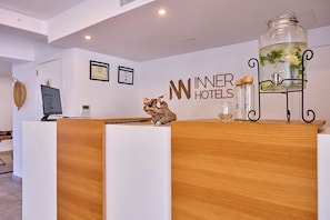 A reception desk with a wooden finish, a framed certificate on the wall, and a decorative jar with a plant on the right. - INNER Hotel Rupit - Adults Only (Santanyi)