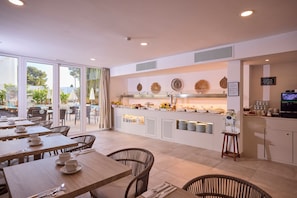 A modern cafe with a glass counter, dining area with wicker chairs, and a view of the outdoors. - INNER Hotel Rupit - Adults Only (Santanyi)