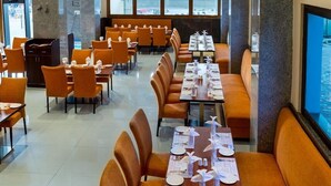 A restaurant with orange seating, tables set with white tablecloths and silverware, and a large window with a view of the outside. - OYO Premium Secunderabad Station (Hyderabad)