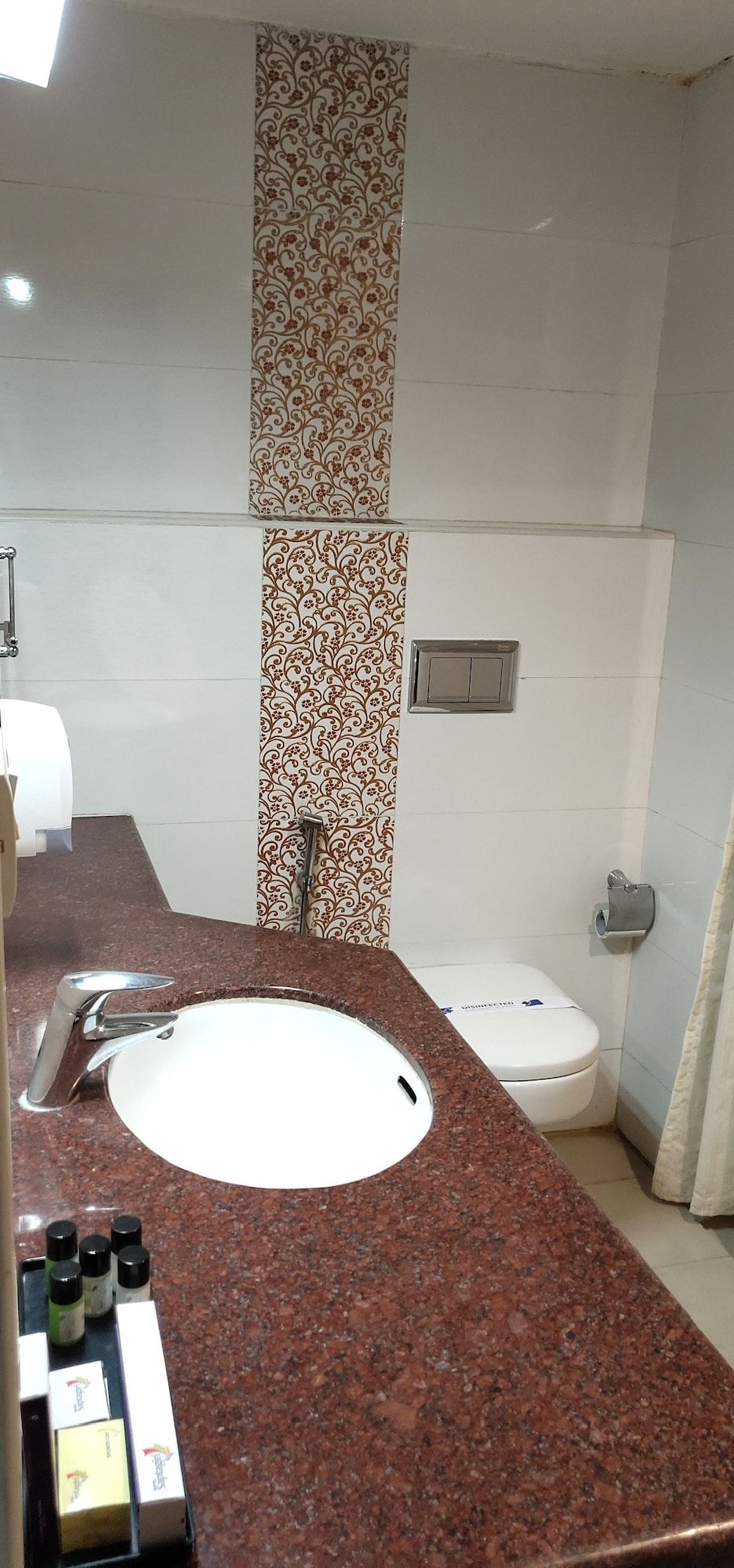 A bathroom with a granite countertop, a white sink, a toilet, and patterned wall tiles.