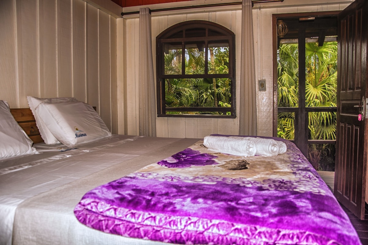 A bedroom with a bed, a window with a view of greenery, and a door.