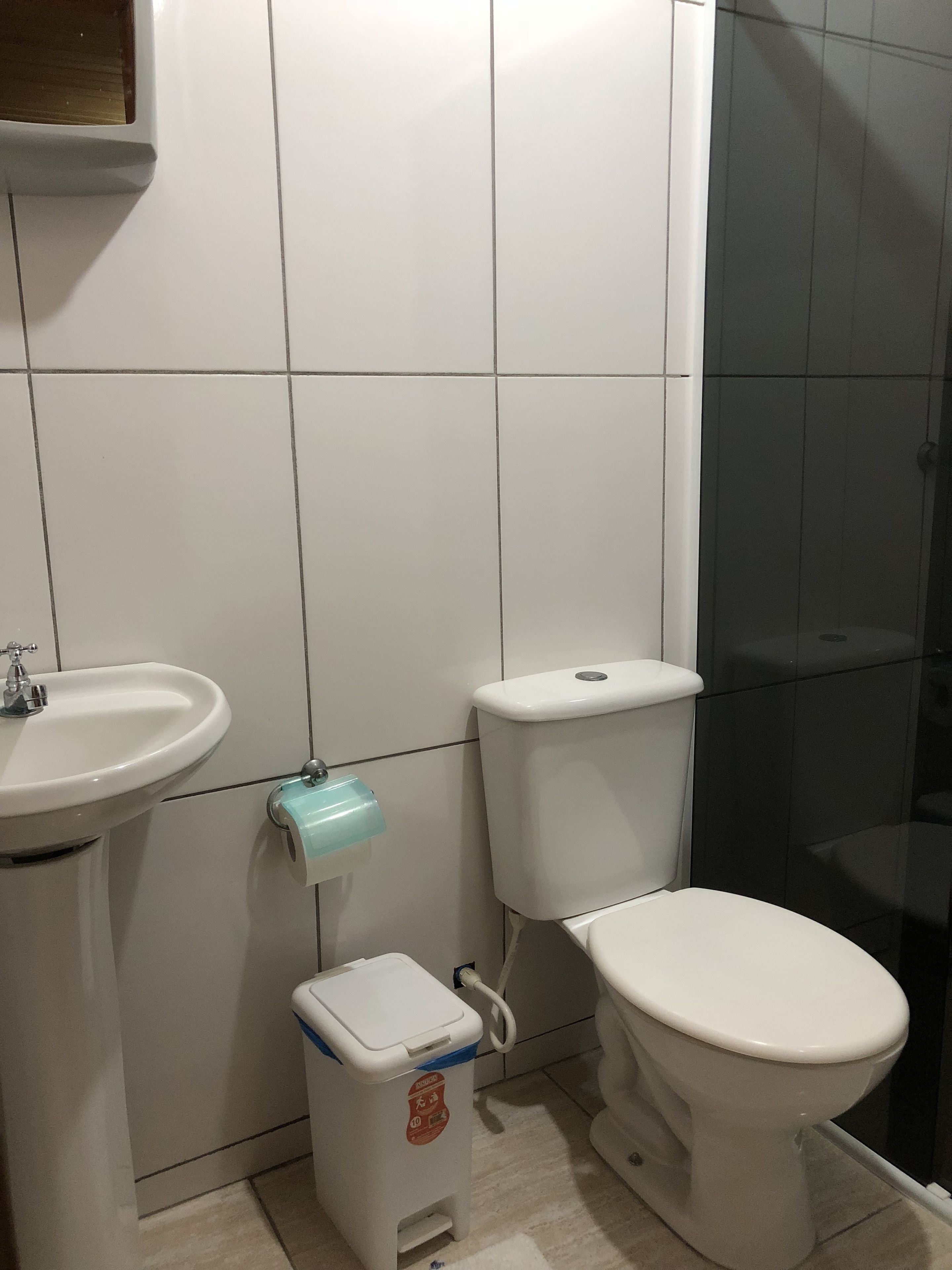 A bathroom with a white sink, toilet, and a trash bin.