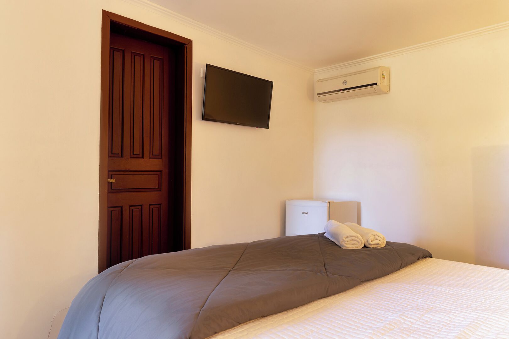 Une chambre d’hôtel avec un lit, une porte en bois, un téléviseur à écran plat et un climatiseur fixé au mur.