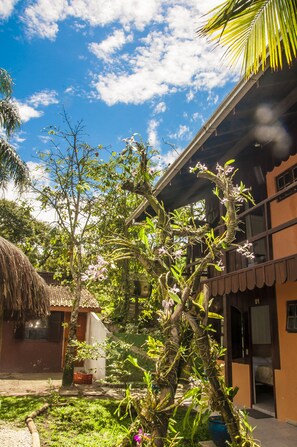 Un jardín tropical con un edificio de techo de paja y una estructura moderna con balcón.