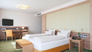 A hotel room with a bed, a desk, a chair, a TV, and a bedside table with a lamp. - Hotel Bildungsblick (Kirchseeon)