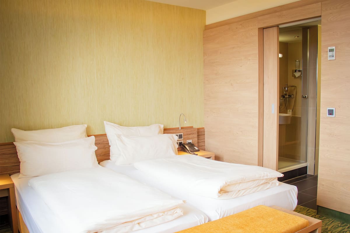 A hotel room with a double bed, a bedside table with a phone, and a shower area.