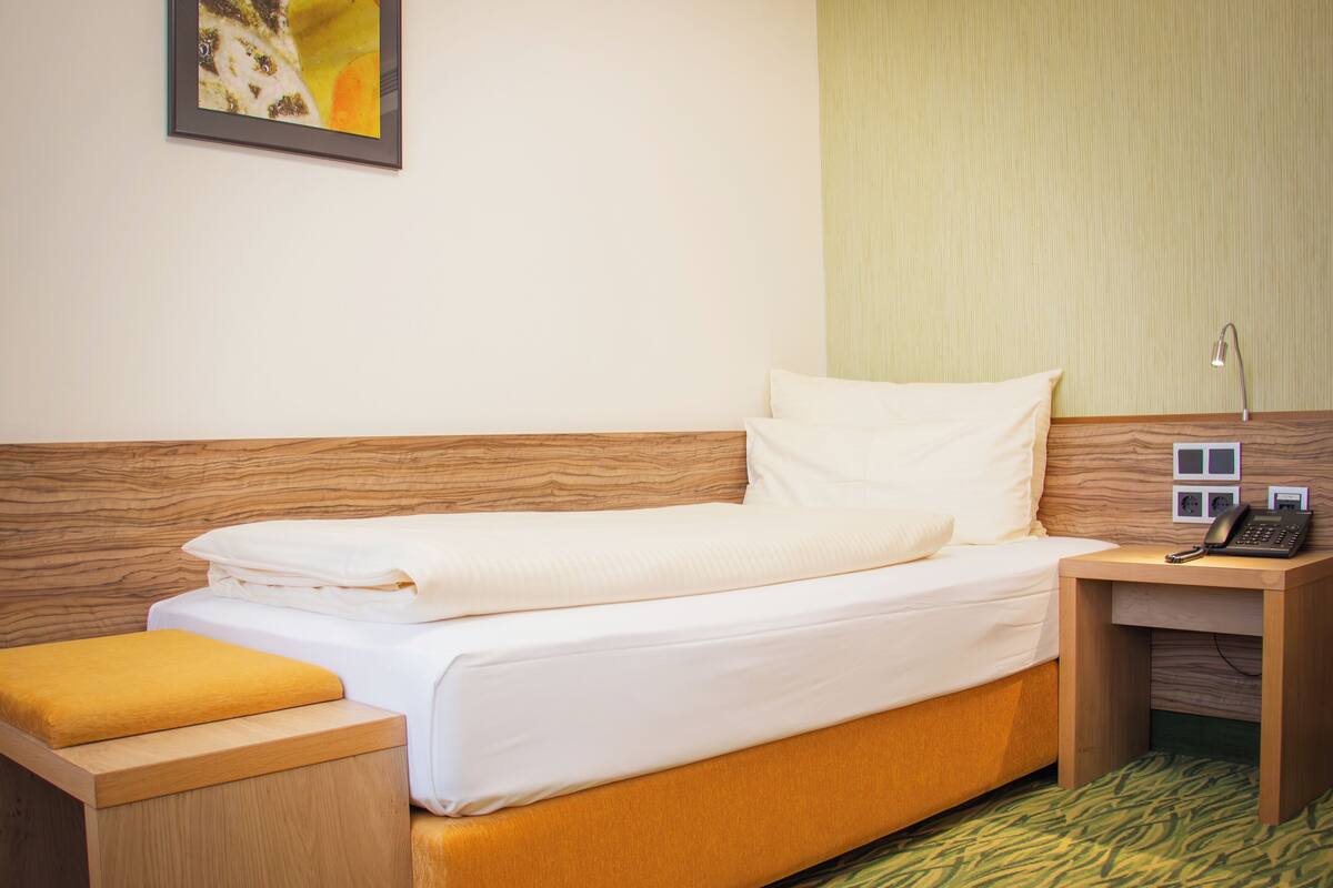 A hotel room with a wooden headboard, a bed with white linens, a bedside table with a lamp, and a telephone.