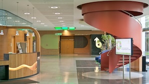 A modern lobby with a wooden reception desk, a spiral staircase, and a sign indicating the direction to the WC. - Hotel Bildungsblick (Kirchseeon)