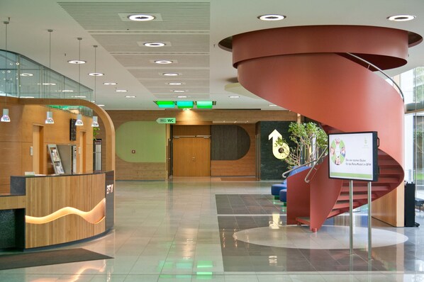 Un vestíbulo moderno con un mostrador de recepción de madera, una escalera en espiral y un cartel que indica el camino al baño.