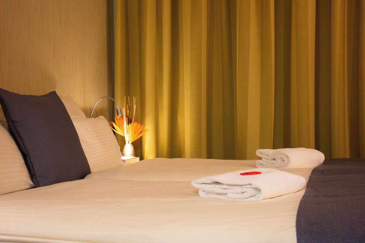 A hotel room with a bed, pillows, a nightstand, and a curtain.