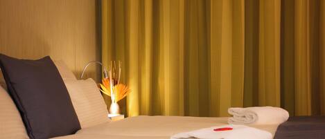 A hotel room with a bed, pillows, a nightstand, and a curtain.