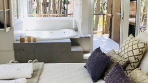 Un dormitorio moderno con un ventanal grande, una bañera integrada y una cama con muchas almohadas.