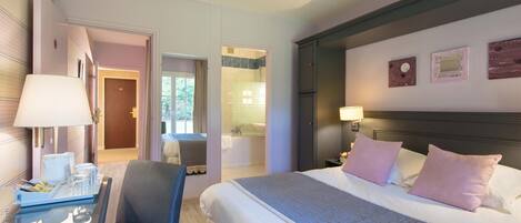 Habitación de hotel con cama, mesita de noche, lámpara, silla y vistas al baño.