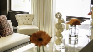 A modern living room with a white sofa, a tufted armchair, and a glass coffee table with vases of flowers. - Hôtel Lensotel (Vendin-le-Vieil)