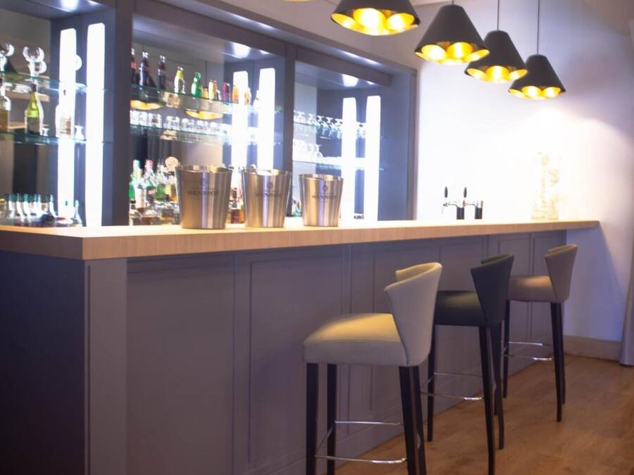 A bar area with a wooden counter, bar stools, and pendant lighting.
