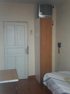 Una habitación con la puerta cerrada, un armario de madera, una cama con colcha a rayas y un televisor montado en la pared.