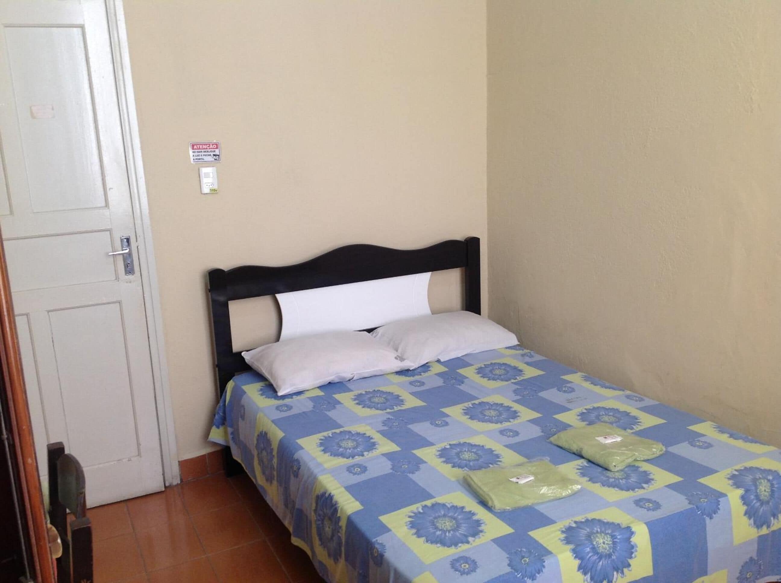 A single bed with a blue and yellow floral bedspread, a white pillow, and a green package on the bed.